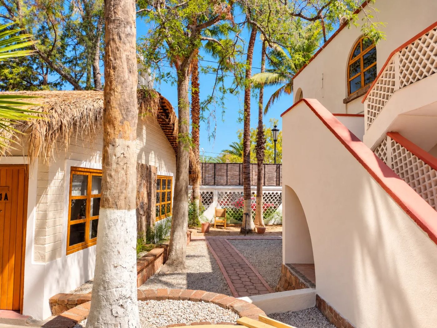 Andador entre palmeras junto a una cabaña de techo de palma y las escaleras de las suites