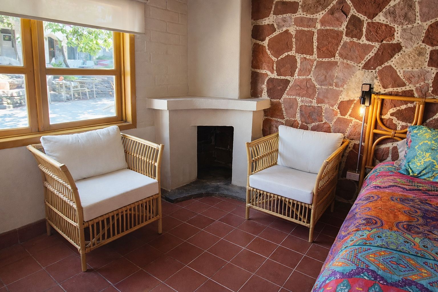 Rincón con dos sillones de ratán junto a una chimenea decorativa blanca y un muro de piedra