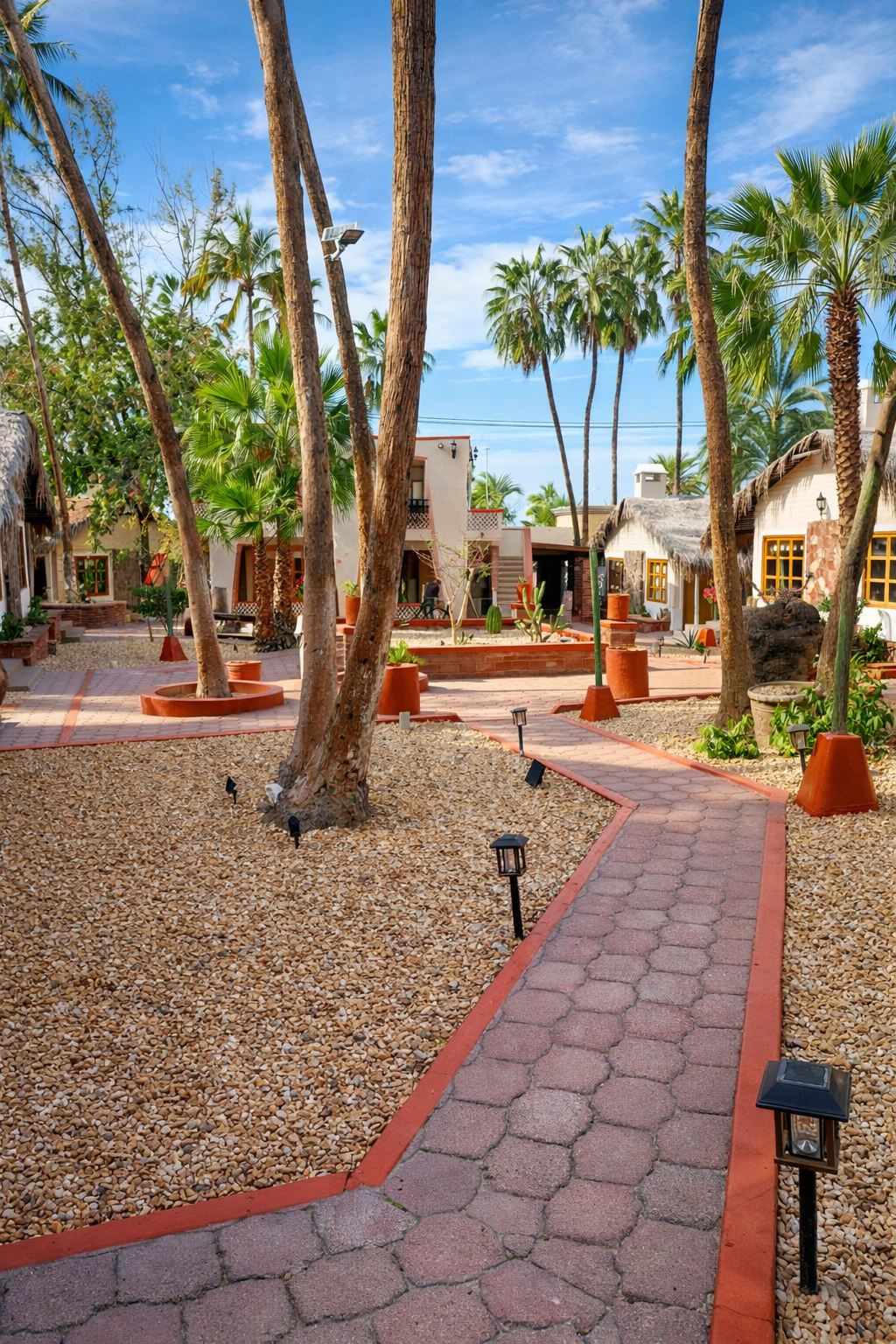 Andador de adoquín entre palmeras y cabañas con techo de palma en el jardín de Sandy Shores